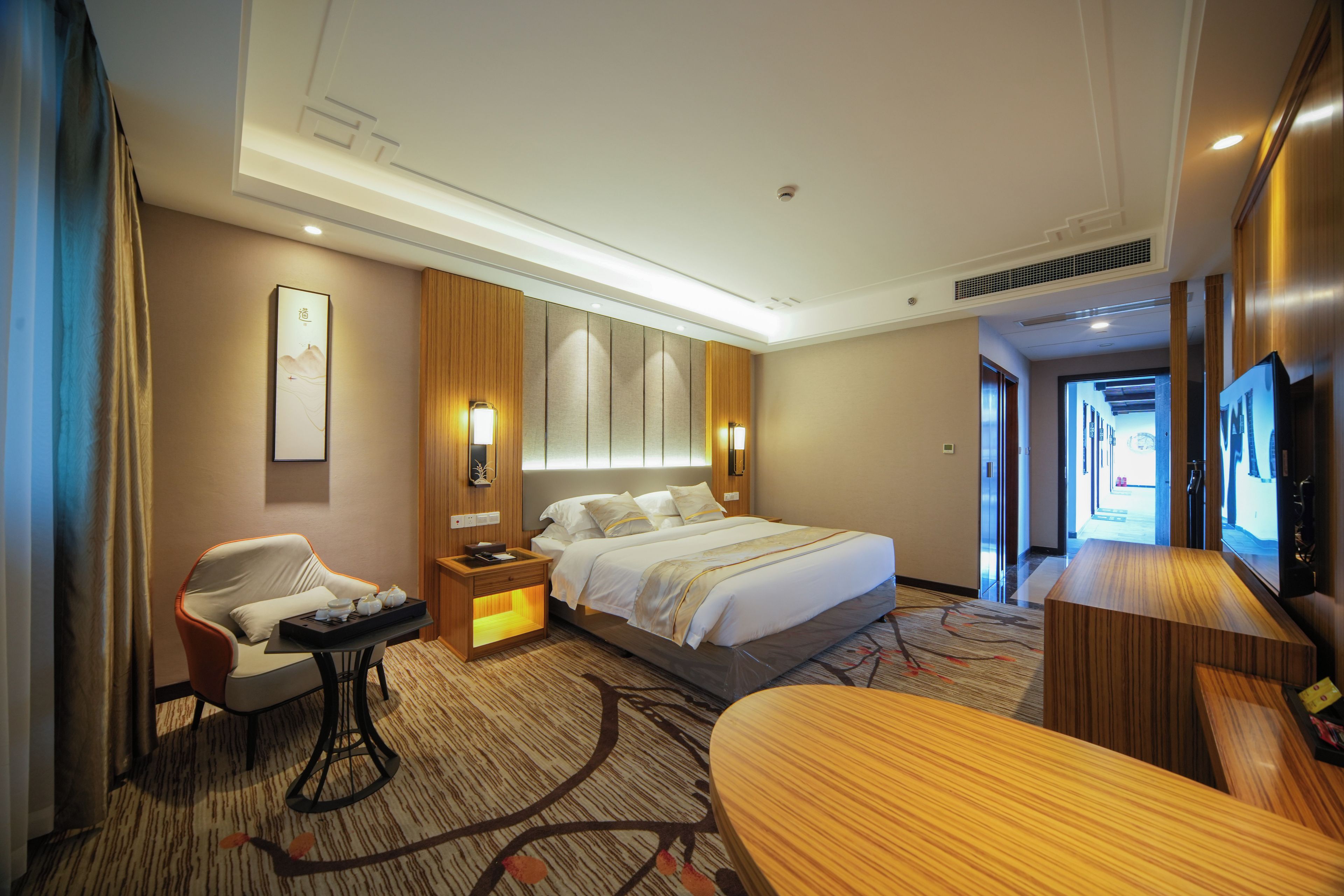 A hotel room with a bed, bedside tables, a desk, a chair, a television, and a painting on the wall.