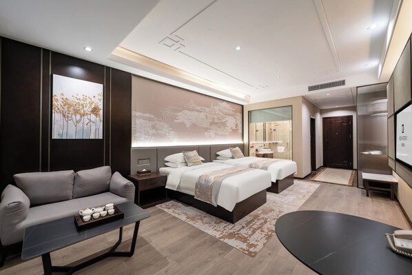 A modern hotel room with a sofa, two beds, a desk, and a bathroom.