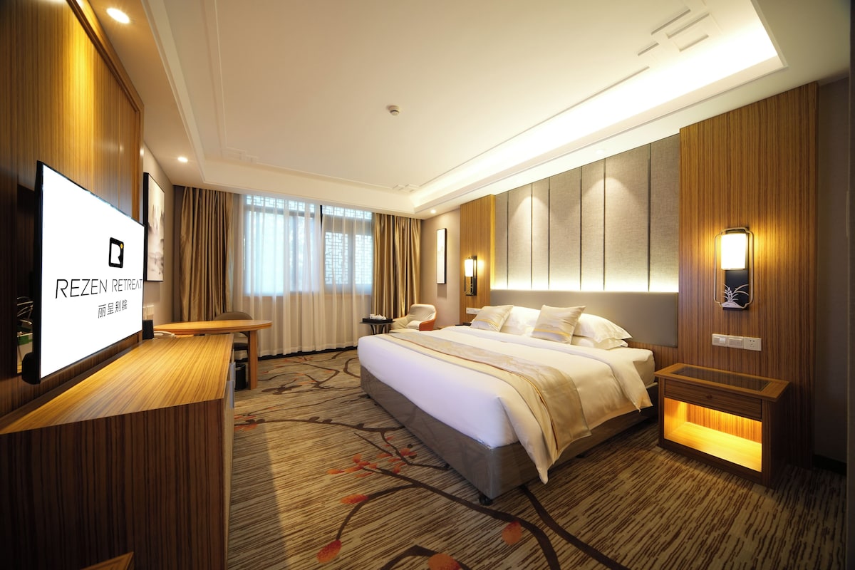 Quarto de hotel com cama, mesas de cabeceira, televisão e vista para o exterior.