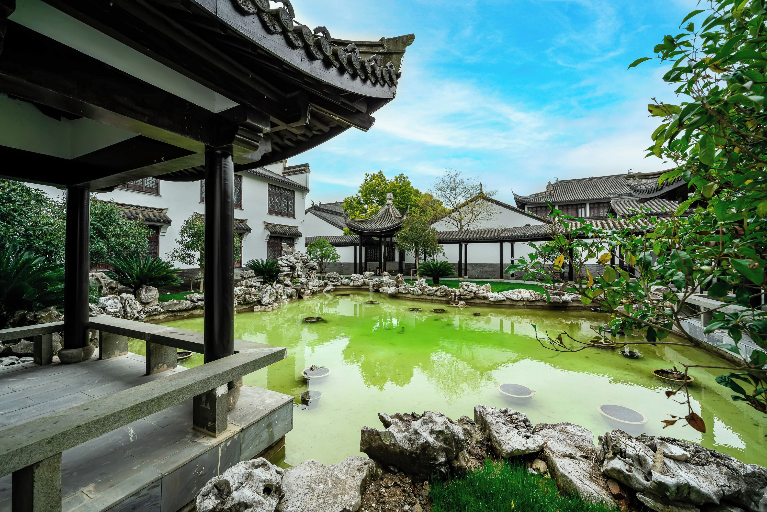 A traditional courtyard with a pond, stone lanterns, and tiled roofs.