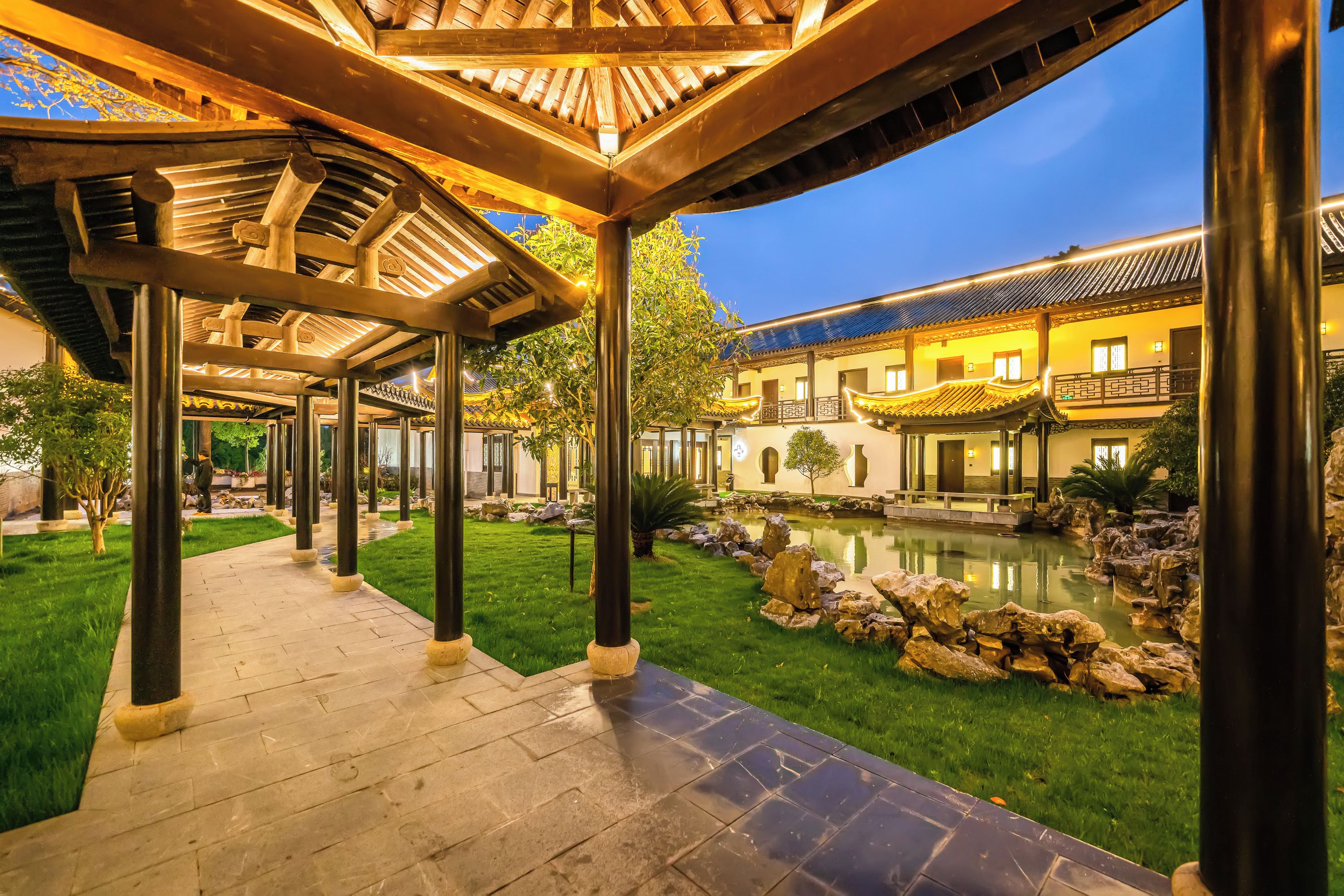 Un patio con una edificación tradicional, un sendero de piedra y un pequeño estanque.