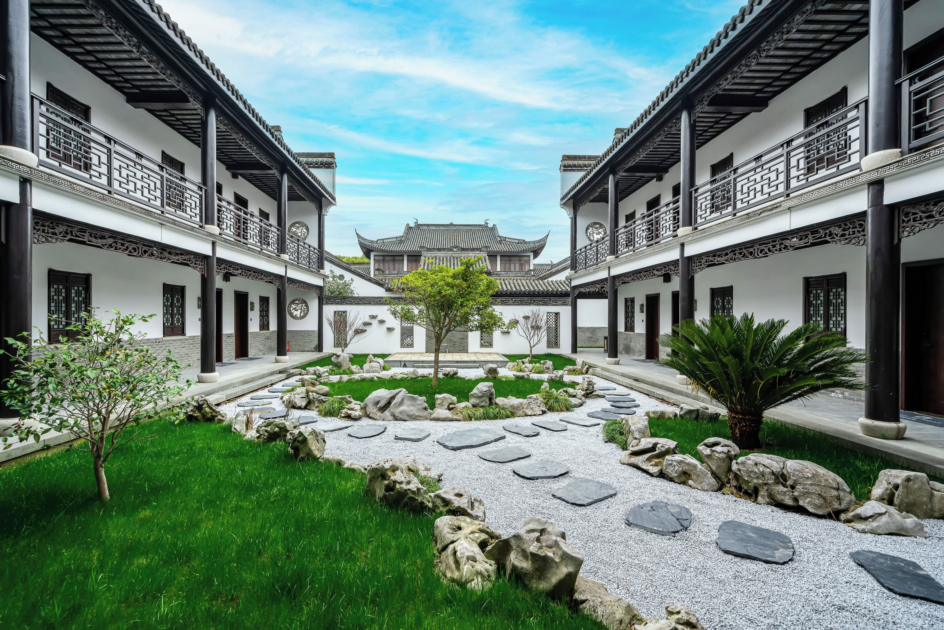 Un patio con arquitectura tradicional, con un jardín central y un sendero, rodeado de edificios con balcones.
