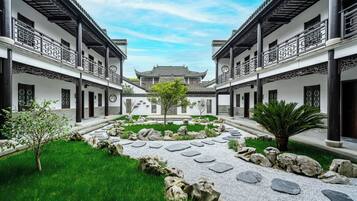 Un patio con arquitectura tradicional, con un jardín central y un sendero, rodeado de edificios con balcones.