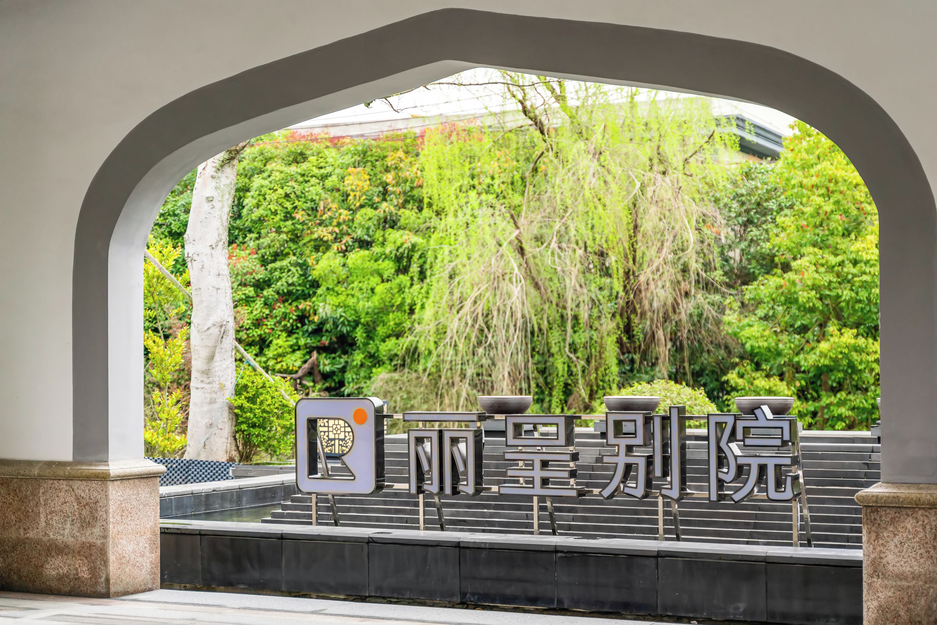 A covered entrance with a view of a lush green garden and a sign with Chinese characters.