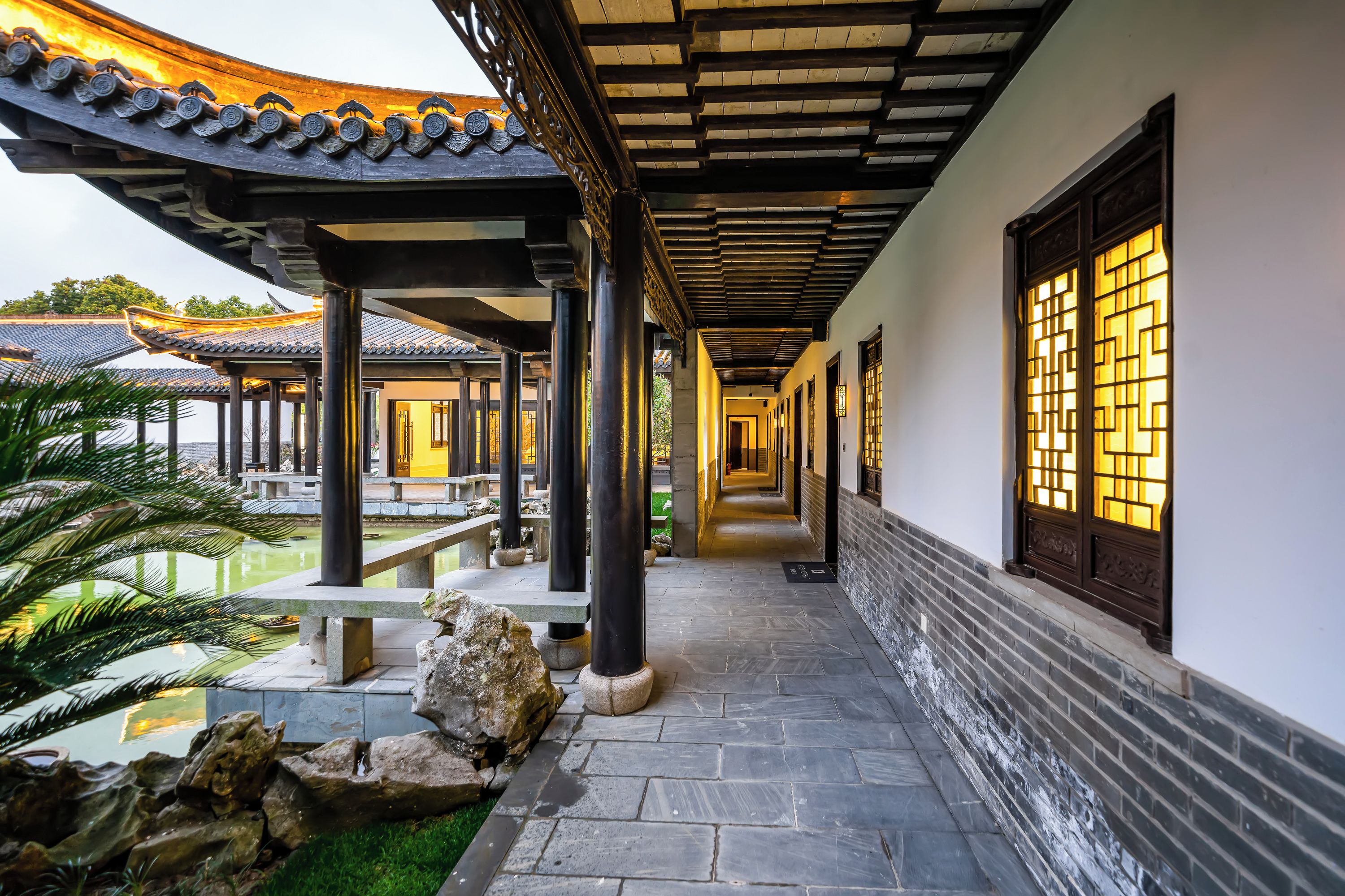A corridor with traditional architecture, stone flooring, and a water feature.