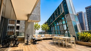 A modern rooftop lounge with exercise equipment, a sofa, and a dining area, overlooking a cityscape. - Designer Duplex PrivatePool, Large Patio (Dubai)