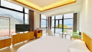 Quarto de hotel moderno com uma cama grande, televisão, uma mesinha e vista para o exterior.