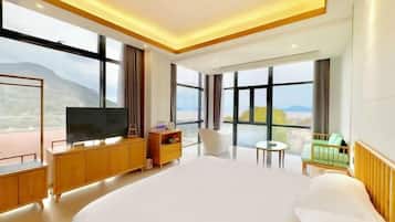 A modern hotel room with a large bed, a television, a small table, and a view of the outdoors.
