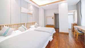 Quarto de hotel com duas camas, piso de madeira, escrivaninha e espelho.