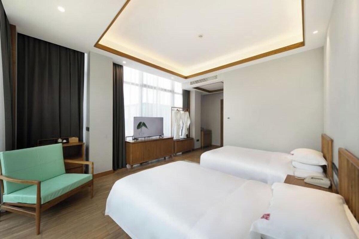 Habitació d'hotel amb dos llits, un escriptori, una cadira, un televisor i una finestra amb cortines.