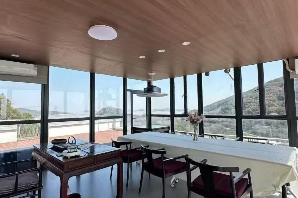 A dining area with a table and chairs, large windows, and a view of the outdoors.