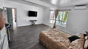 A bedroom with a bed, a TV mounted on the wall, a window with curtains, and a wooden floor. - Moon Mirror (Tijuana)