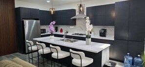 A modern kitchen with dark cabinetry, a stainless steel refrigerator, a central island with bar stools, and a gas stove. - Moon Mirror (Tijuana)