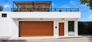 A modern two-story building with a garage door, a wooden door, and a balcony with plants. - Moon Mirror (Tijuana)