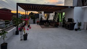 A rooftop patio with potted plants, outdoor furniture, and a barbecue grill.