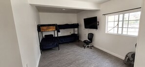 A room with a bunk bed, a desk with a chair, a TV, and a window.