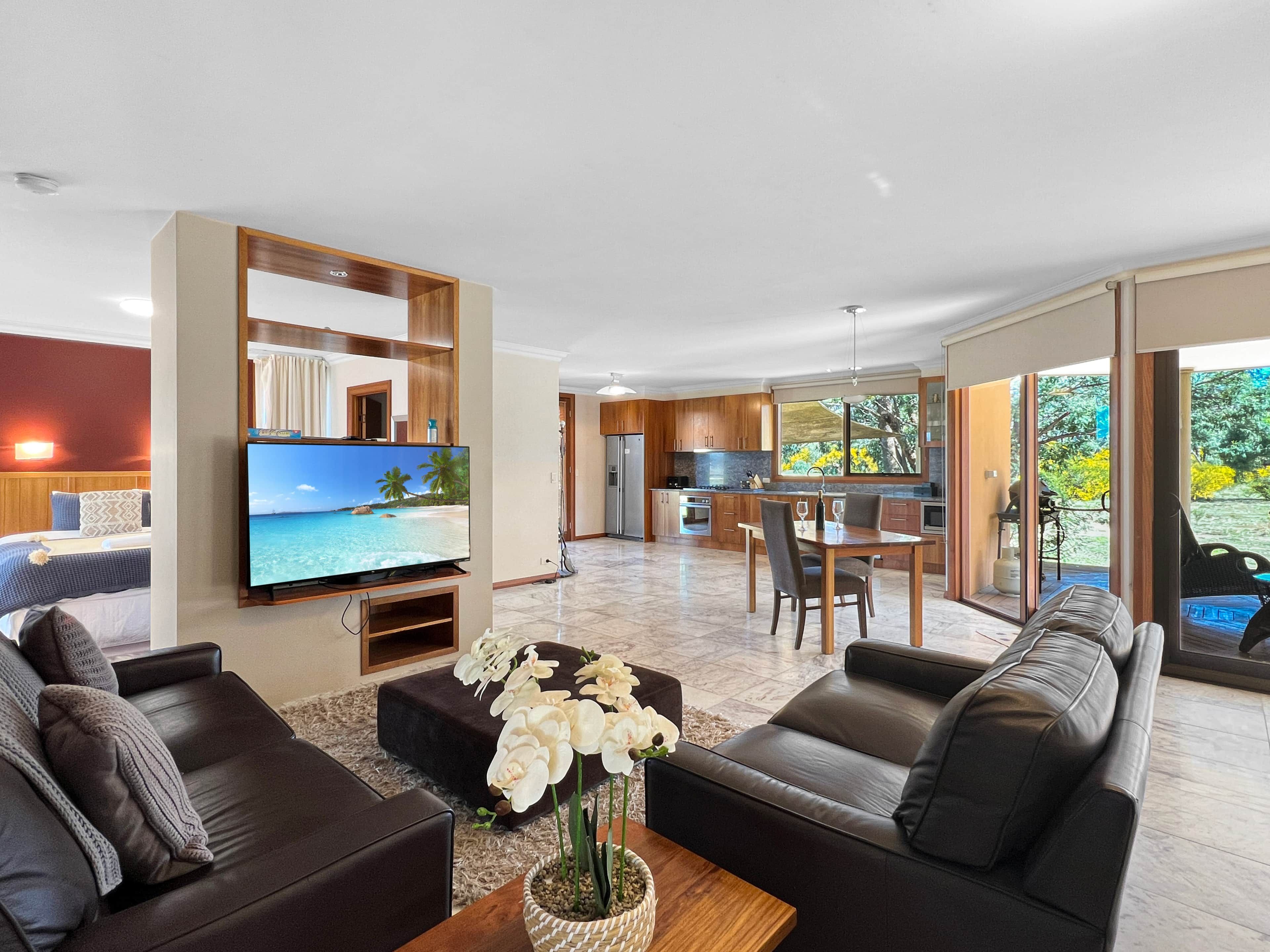 A modern living room with a flat-screen TV, leather sofas, a coffee table, and a dining area with a table and chairs.