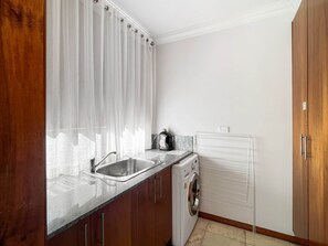 Una cocina compacta con un lavamanos de acero inoxidable, lavadora integrada y salpicadero de azulejos blancos.