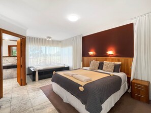 Una habitación de hotel con una cama, mesitas de noche, un escritorio, un ventanal con cortinas y vistas al exterior.