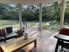 A covered outdoor patio with a wooden table and seating area, surrounded by greenery and trees.