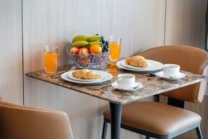 Una mesa de desayuno con cruasanes, fruta, jugo y tazas de café.