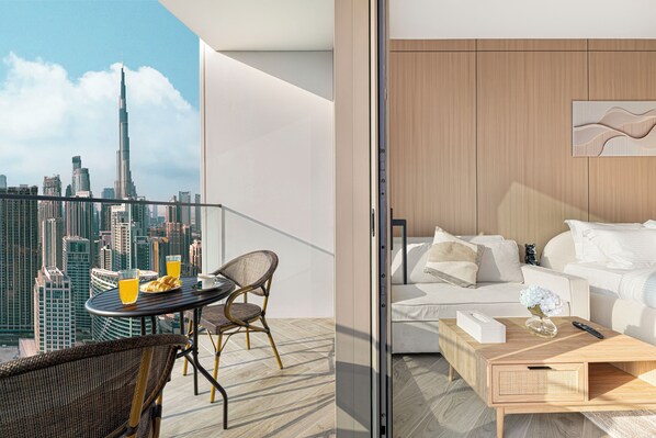 Habitación de hotel moderna con balcón y vistas a un paisaje urbano, incluyendo un rascacielos destacado.