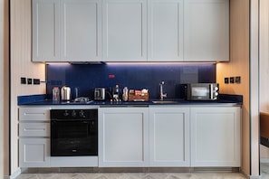 Una cocina moderna con armarios blancos, un horno negro, un microondas y una barra para café.
