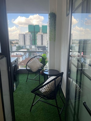 A balcony with artificial grass, two black chairs, a small table, and a view of buildings. - Get to experience ultimate luxury in the heart of Nairobi. (Nairobi)