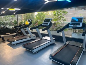 A gym with treadmills, exercise bikes, and a large window with a view of greenery. - Get to experience ultimate luxury in the heart of Nairobi. (Nairobi)