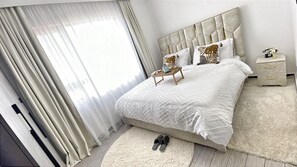 A bedroom with a bed, bedside tables, a nightstand, a chair, and a window with curtains. - Get to experience ultimate luxury in the heart of Nairobi. (Nairobi)