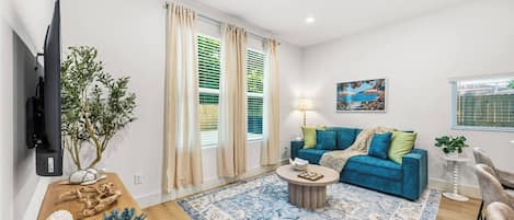 A living room with a blue sofa, a coffee table, a TV mounted on the wall, and a plant.