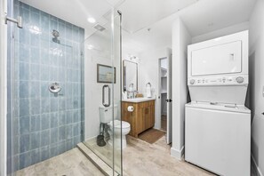 Et moderne badeværelse med en glasafskærmet brusekabine, toilet, vask med et træskab og en indbygget vaskemaskine.