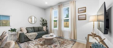 A modern living room with a sofa, coffee table, and a large window with curtains.