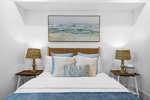 A bedroom with a bed, two nightstands, a headboard, a framed picture above the bed, and two lamps on the nightstands.