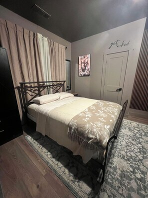 A bedroom with a bed, curtains, a door, and a wall with a poster. - Studio  located inside Paradise Valley Resort & Club. A Clothing Optional Club. (Dawsonville)