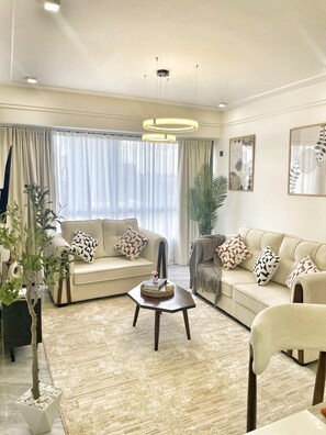 A modern living room with two sofas, a coffee table, and a large window with curtains. - Urban n modern unit just in the heart of Nairobi. (Nairobi)