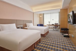 Habitación de hotel con dos camas, un escritorio, una silla, un televisor y una alfombra estampada.
