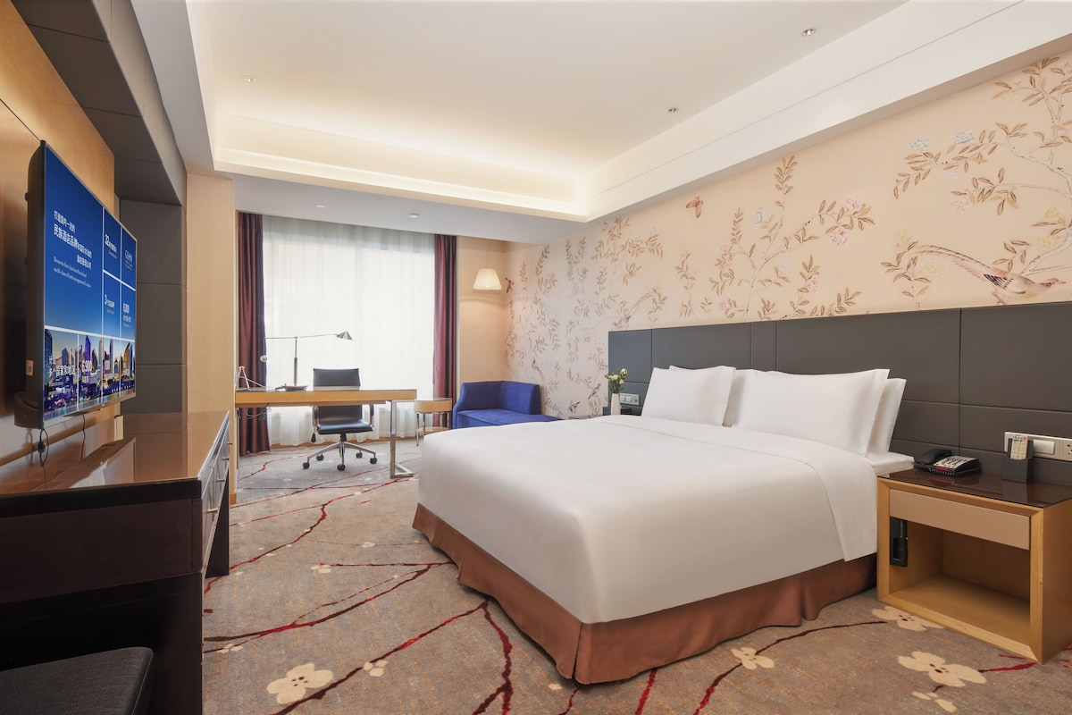 Habitación de hotel con una cama grande, un escritorio, una silla, un televisor y un detalle decorativo en la pared.