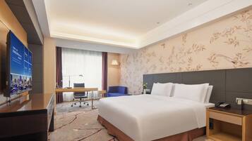 A hotel room with a large bed, a desk, a chair, a TV, and a decorative wall.