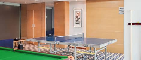 A ping pong table with a pool table in the foreground, a framed artwork on the wall, and a door with a sign.