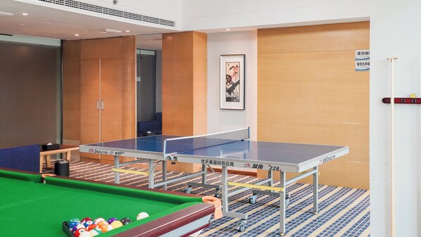 A ping pong table with a pool table in the foreground, a framed artwork on the wall, and a door with a sign.
