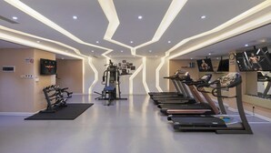 Un gimnasio moderno con cintas de correr, máquinas de pesas y un televisor montado en la pared.