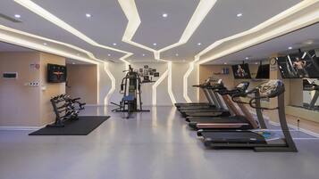 Un gimnasio moderno con cintas de correr, máquinas de pesas y un televisor montado en la pared.