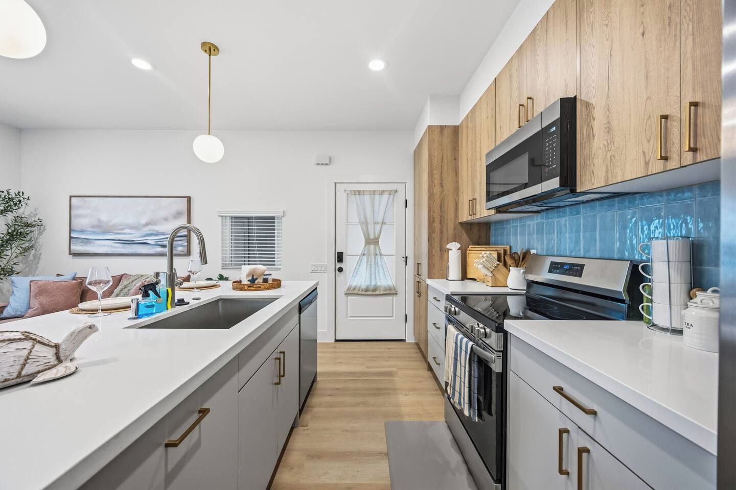 Une cuisine moderne avec des plans de travail blancs, des meubles en bois, un four encastré et un four à micro-ondes.