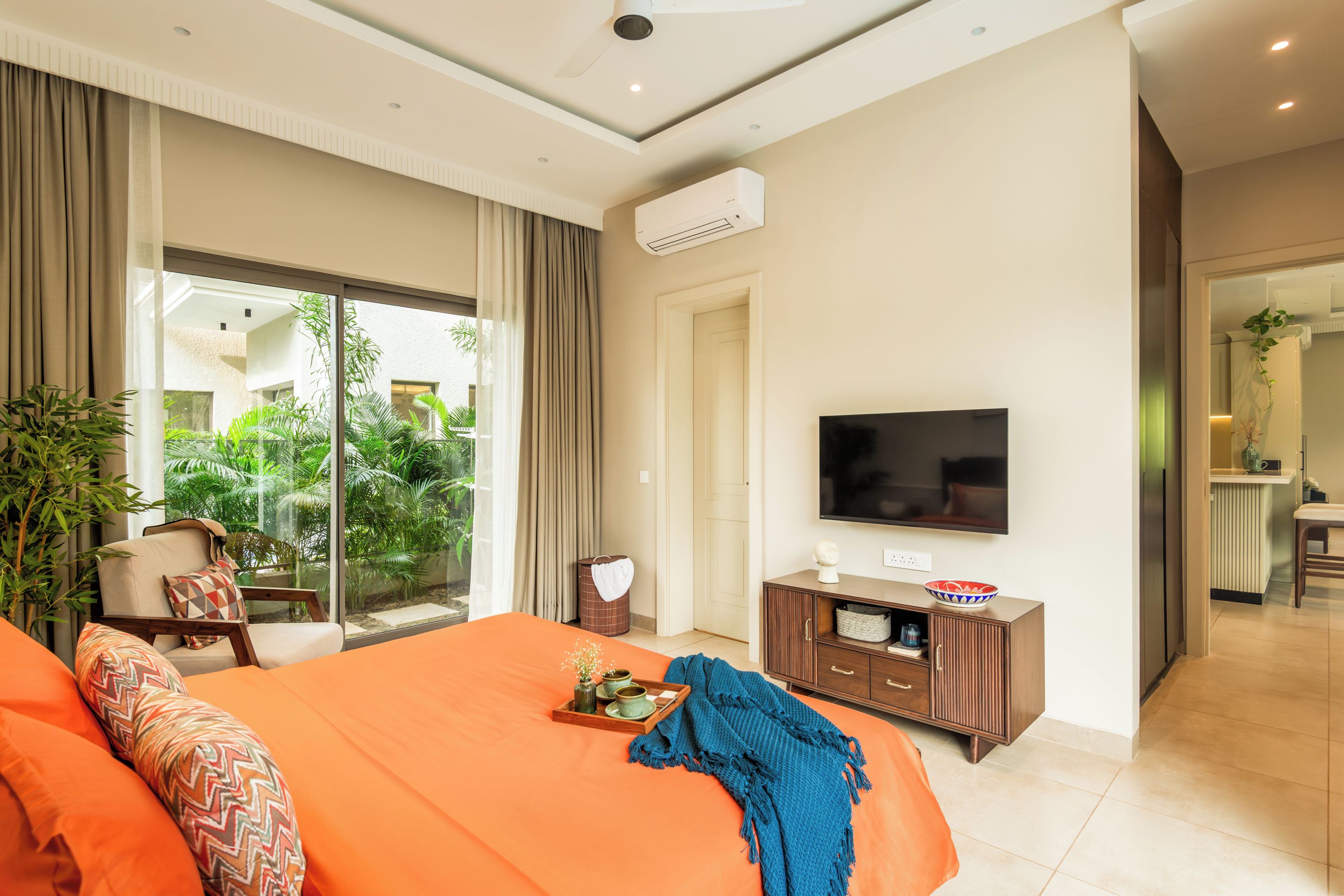 Una camera d'hotel con un letto, una televisione, un piccolo armadio e vista su un giardino attraverso la finestra.