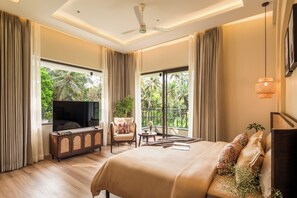 A hotel room with a large bed, a TV, a seating area with a chair and table, and a balcony with a view of greenery. - Paddy Field View 5 Mins Drive to Beach  (Goa)