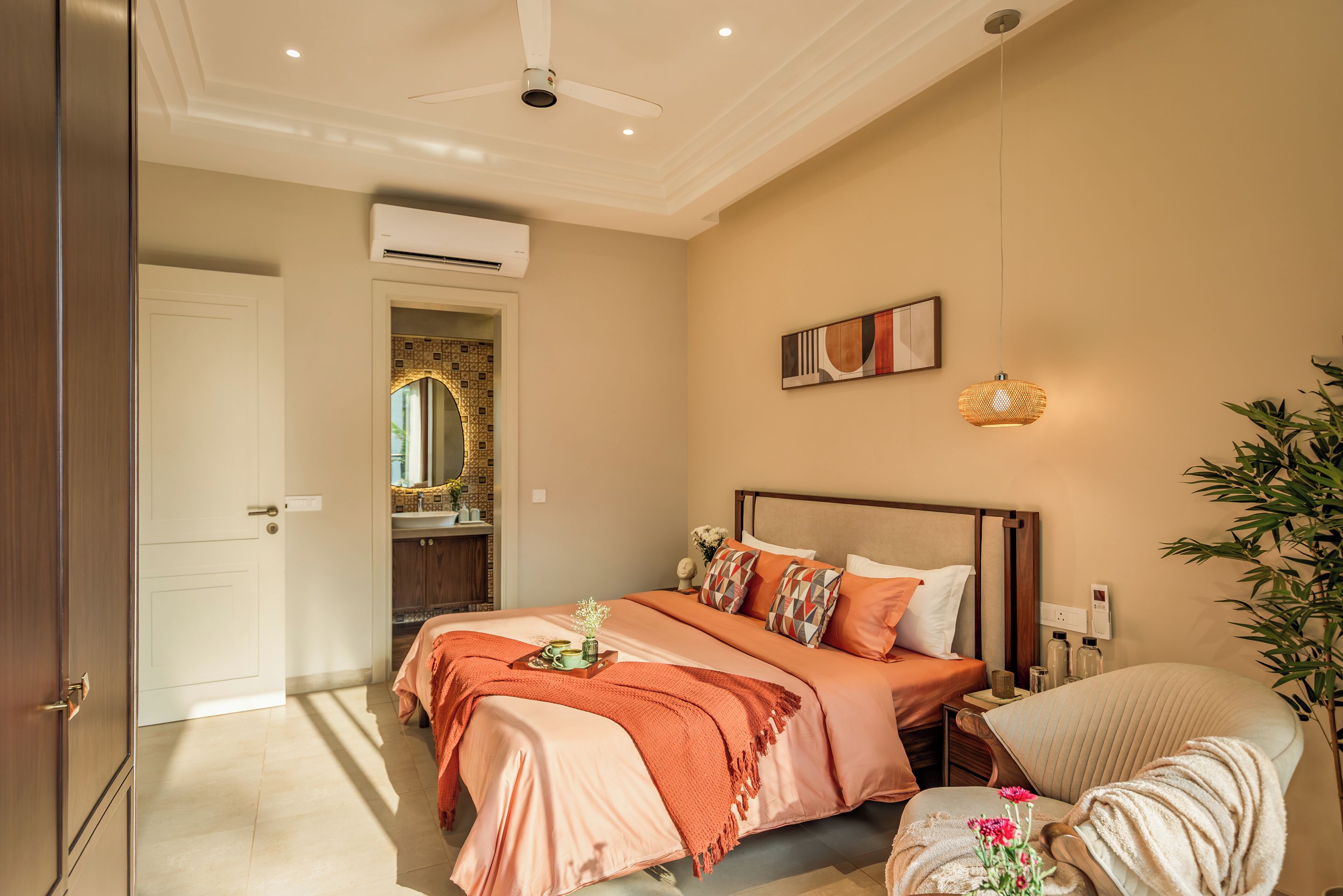 A hotel room with a bed, a bedside table, a chair, a mirror, an air conditioning unit, and a wall-mounted artwork.