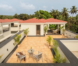 Un patio en la azotea con mobiliario exterior, rodeado de abundante vegetación y palmeras.