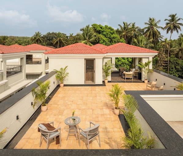 A rooftop patio with outdoor furniture, surrounded by lush greenery and palm trees.