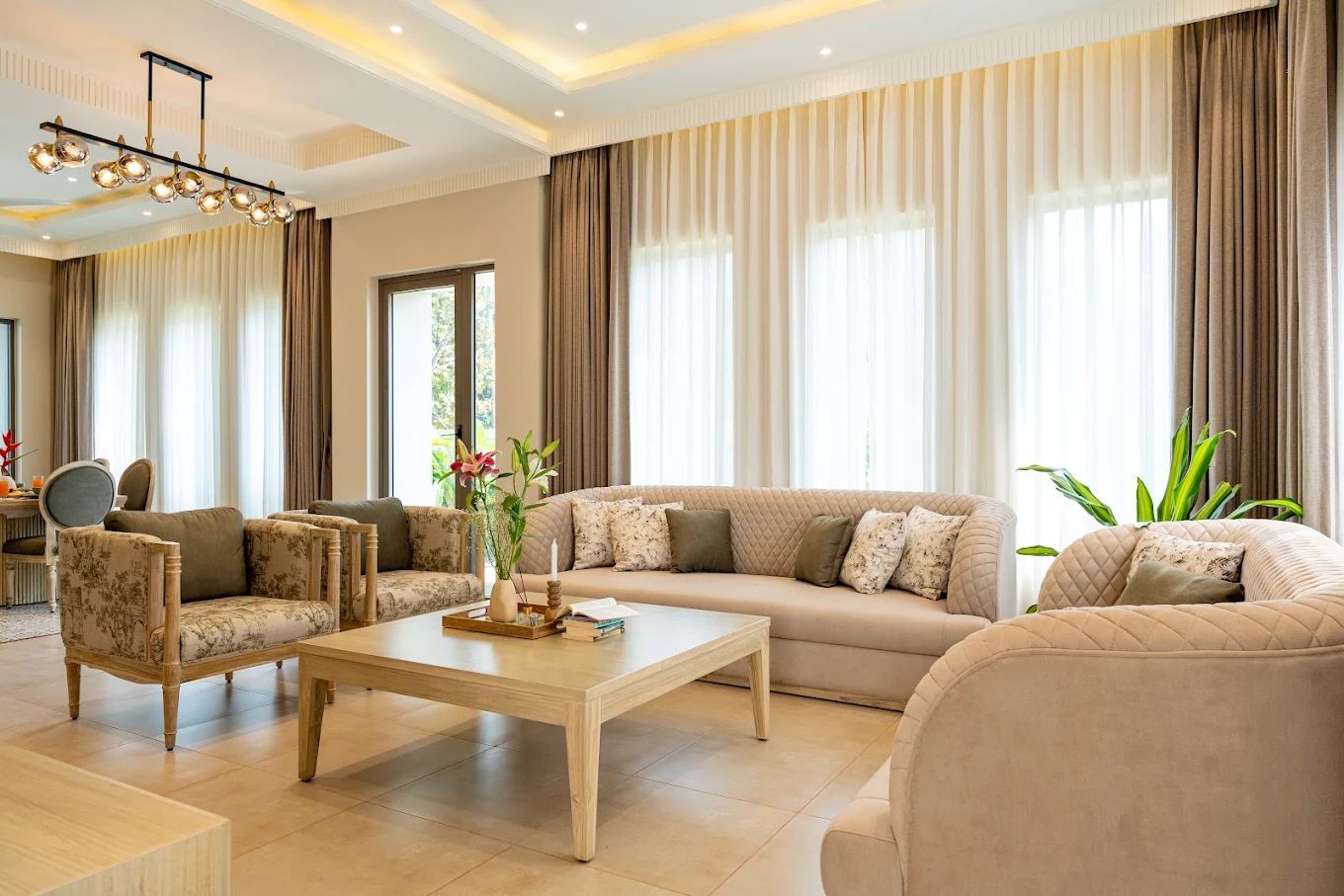 Uma sala de estar ampla com sofá, poltronas, mesa de centro e lustre.